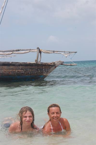 Mother and daughter swim in turquoise water in front of an old wooden dhow