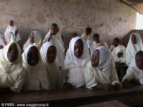 Children wrapped in white shawls sitting at desks in a classroom
