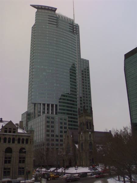 Glass skyscraper with spire beside stone cathedral, snowy streets under grey sky
