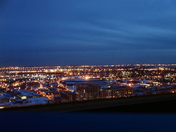 City lights glowing at dusk seen from a high floor, orange lights under blue sky