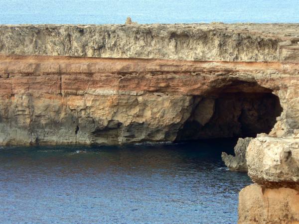 Sea cave carved into limestone cliffs above blue water, Malta
