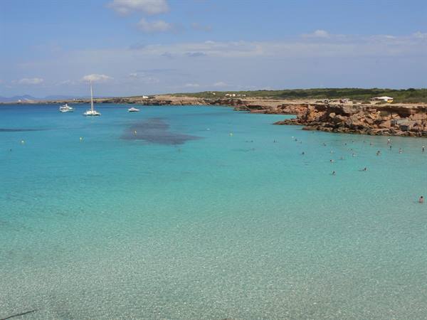 Swimmers in turquoise water with sailboats, rocky cliffs of Cala Saona