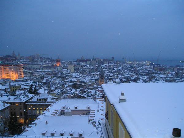 Snow-covered rooftops of Genoa at dusk, snowfall over the city and harbor