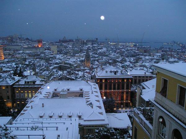 Snow-covered rooftops of Genoa at dusk, the harbor glittering in the distance