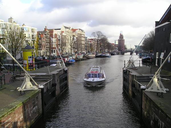 Tour boat crossing an Amsterdam canal between brick houses and drawbridge