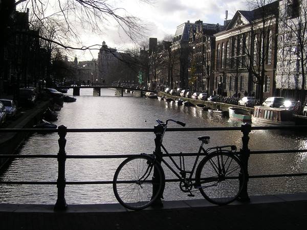Bicycle leaning on a bridge railing over an Amsterdam canal