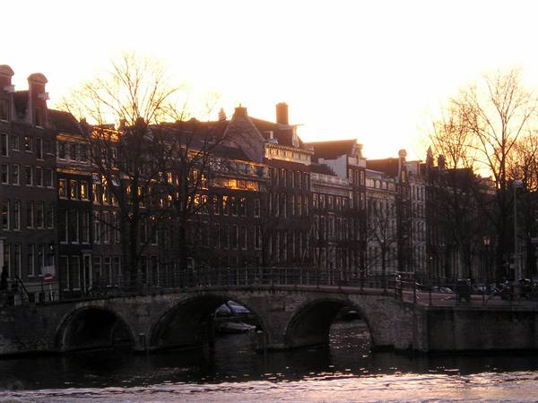 Brick bridge over Amsterdam canals, Dutch houses lit by low sunlight