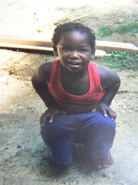 Smiling girl squatting on bare ground, red tank top and blue pants