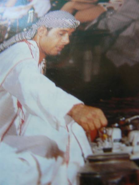Man in white thobe and keffiyeh pouring tea from a kettle
