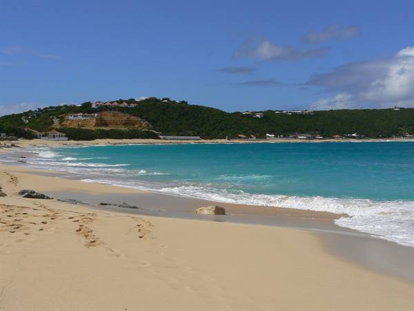Turquoise waves breaking on golden sand in front of green hills with houses