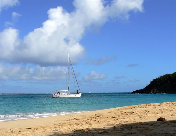 White sailboat anchored in turquoise water, sandy beach and green rocky headland
