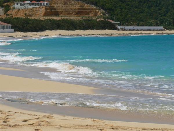 Turquoise waves break on golden sand, houses on the green hill