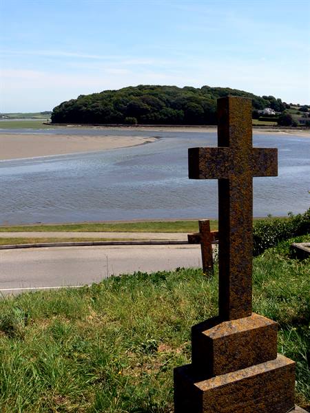 Granite cross on grass overlooking a bay with wooded island