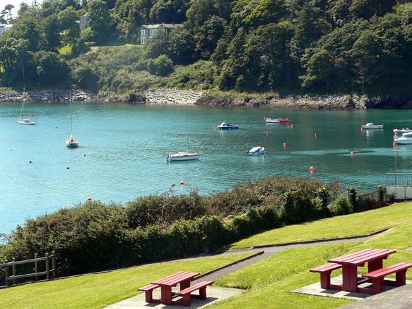 Boats moored in an emerald-green cove, red picnic tables on the lawn