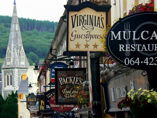 Pub and restaurant signs hanging over a street with a church spire