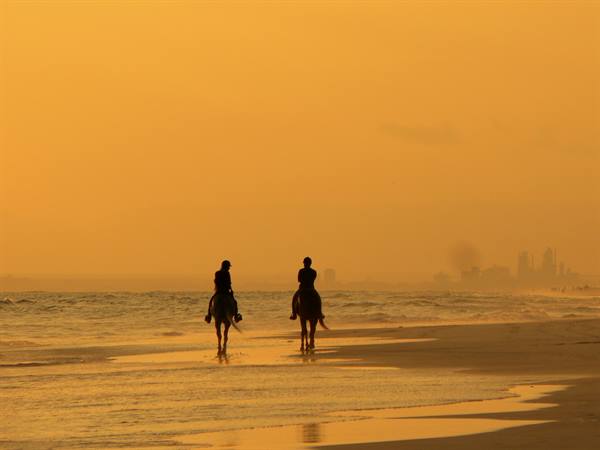 Two horse riders on the wet beach, golden light, hazy skyscrapers in the distance