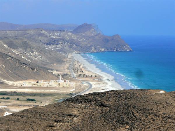 Sandy beach between arid mountains and turquoise sea, coastal road with sparse vegetation