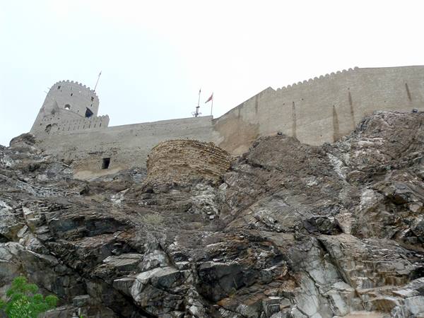 Old stone fortress with tower and walls on rocks under white sky