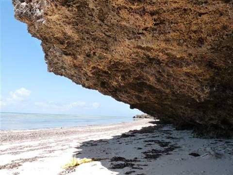 Large coral rock overhangs white sand beach and turquoise sea