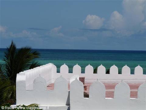 White terrace with arabesque battlements above the turquoise ocean and palms