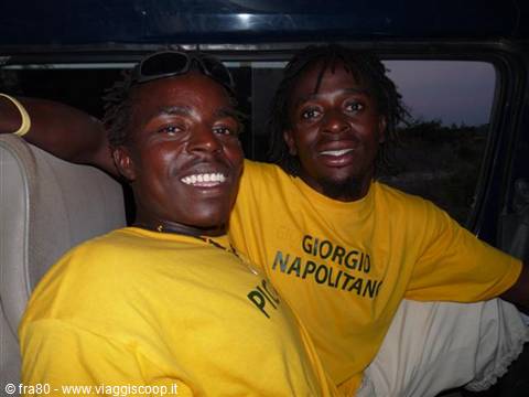 Two smiling young men in yellow shirts inside a bus at dusk