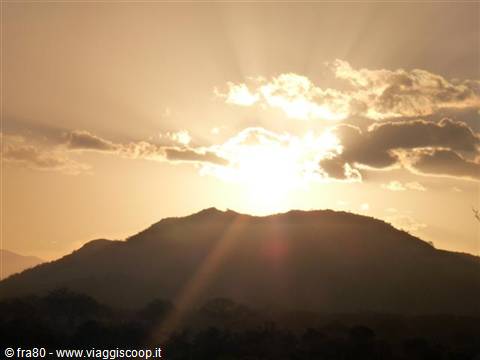The sun glows behind the dark silhouette of a mountain among golden clouds
