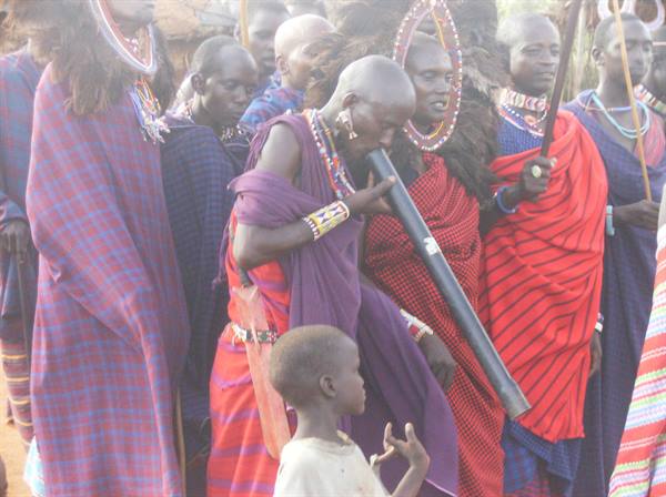 Maasai woman blows a horn during a gathering, men in red shukas