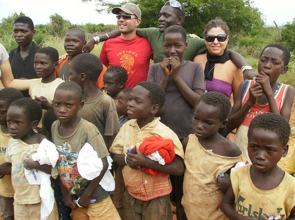 Two smiling tourists embrace a group of local children in daylight