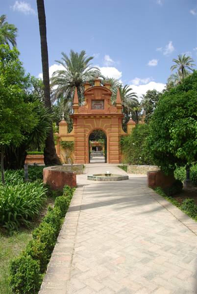 Brick gateway among palm trees, paved path, circular fountain in sunlight