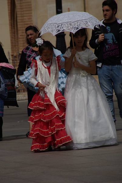 Girl in red ruffled flamenco dress beside girl in white with lace parasol