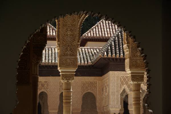 Carved columns and tiled roofs seen through a Moorish arch of the Alhambra
