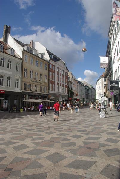 Pedestrian square with diamond-patterned paving, colorful buildings and people under blue sky