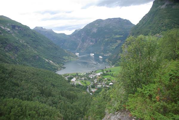 Geiranger fjord with cruise ships between green mountains and village below
