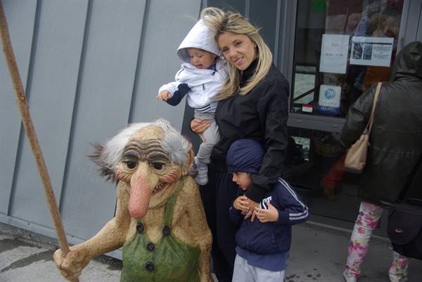 Mother with two children beside a large wooden troll statue
