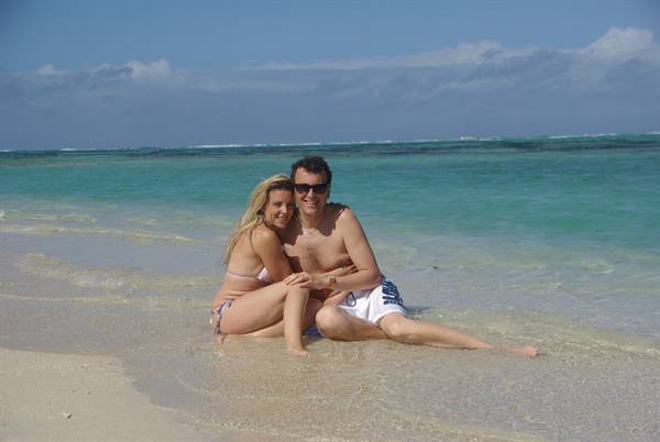 Couple in swimwear sitting on wet sand in front of turquoise sea