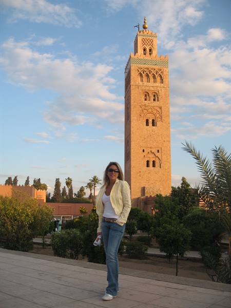 Smiling woman in front of the Koutoubia minaret among palms and gardens