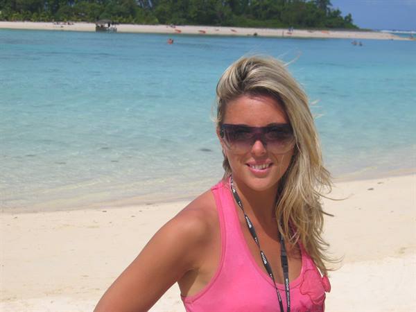 Blonde woman in dark sunglasses and pink top on white sand beach