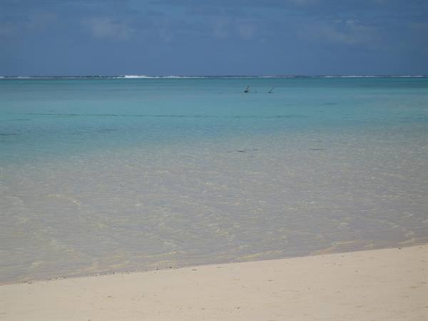 White sand and shallow turquoise sea, distant fishermen, cloudy sky