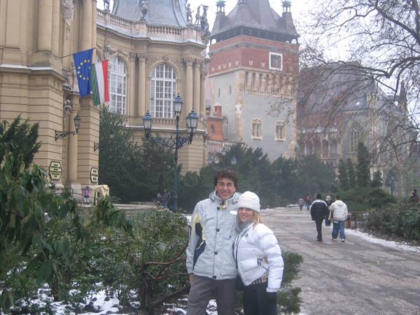 Smiling couple in front of Vajdahunyad Castle, snow on ground, flags waving