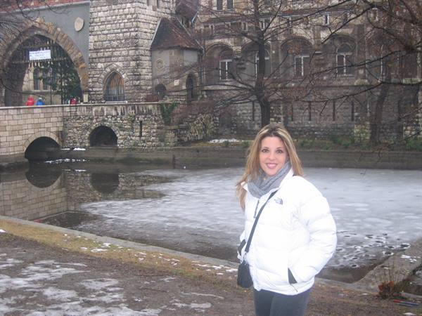 Smiling woman in white down jacket in front of Vajdahunyad Castle and frozen pond