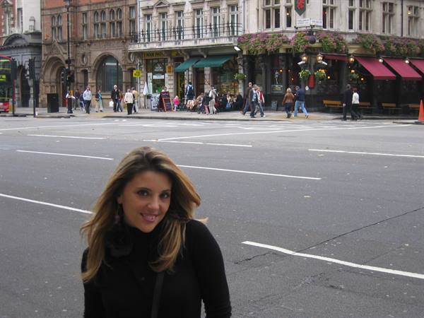 Smiling woman crossing the asphalt in front of London pubs with red awnings