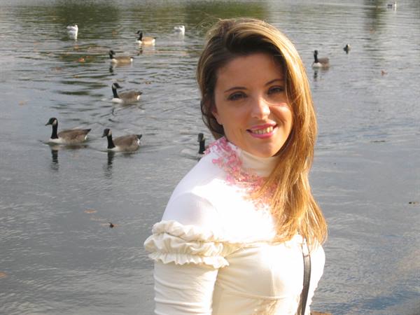 Blonde woman smiling in front of a lake with swimming Canada geese