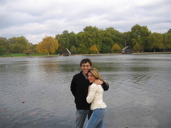 Couple embracing by the Serpentine lake in Hyde Park, wooden boathouses behind