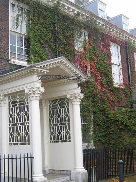 White neoclassical columned portico in front of red brick covered with ivy