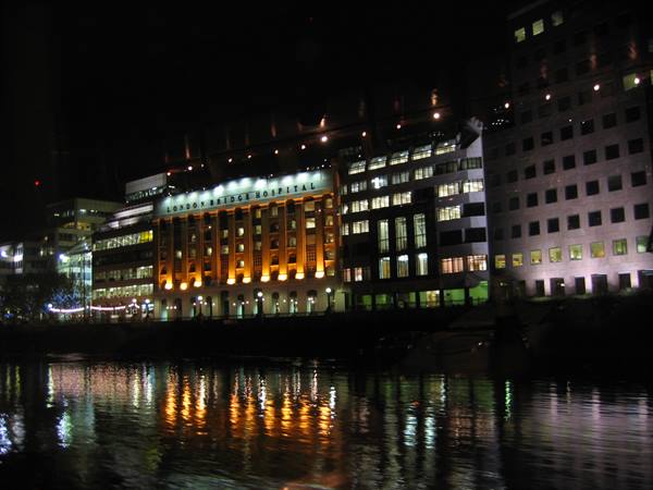 Illuminated hospital building along the river at night, lights reflected on water