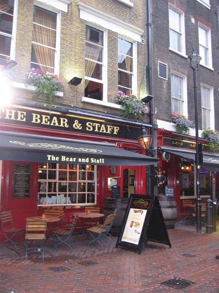 Pub with golden sign, window flowers and outdoor chairs on cobblestone street