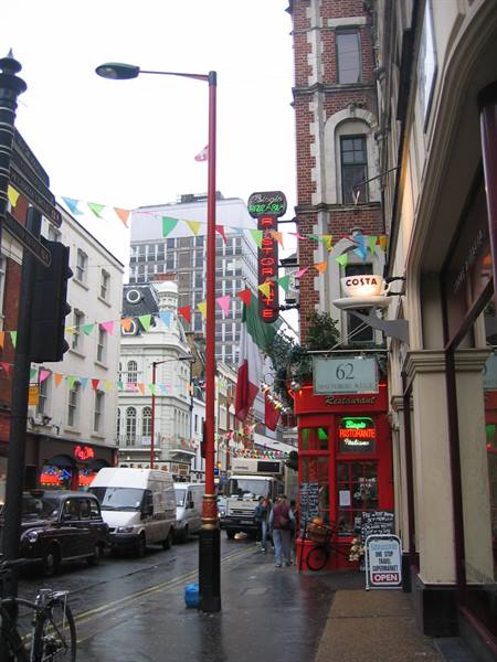 City street with colorful bunting, red restaurant, traffic and pedestrians under gray sky