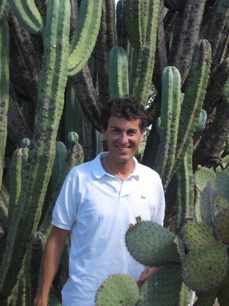 Smiling man in white polo shirt among tall columnar cacti and prickly pears
