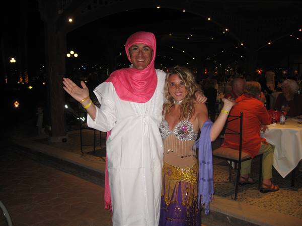Man in white galabeya with pink headscarf beside a belly dancer