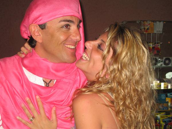 Man in pink turban smiles as a blonde woman kisses his cheek at a kiosk